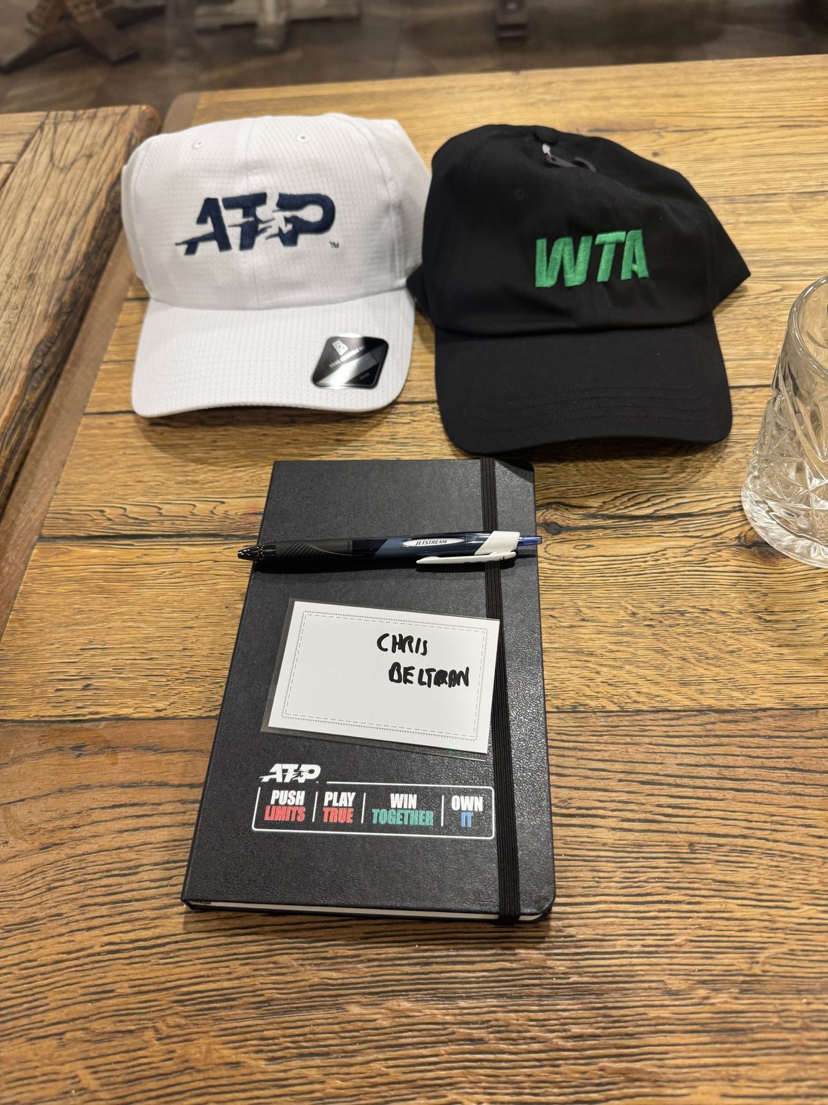 ATP and WTA caps beside a notebook with Chris Beltran's name badge